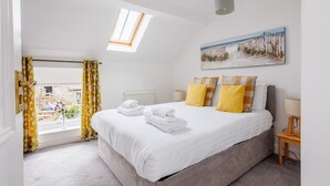 A bedroom with a large bed, a skylight, a painting, and a view of the outside. - Ty Mabon: 1‑Bed First-Floor Apartment in Aberffraw | Managed by Anglesey Holiday Lettings (Ty Croes)