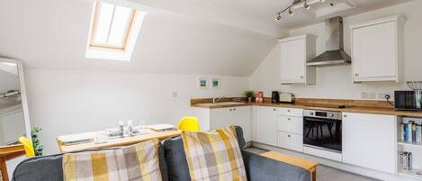 A compact living space with a kitchenette, a sofa with plaid cushions, a dining table, and a small window.