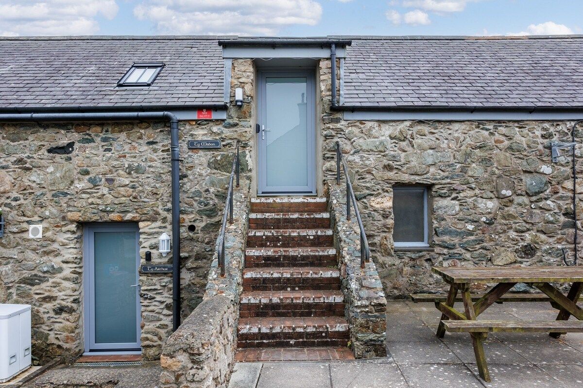 A stone building with a staircase leading to a door, a small window, and a picnic table.