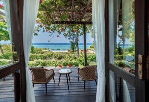 A wooden deck with wicker chairs and a small table, overlooking a lush garden and the ocean. - PARADISE - Four Bedroom Villa, Sleeps 9 (Zanzibar)