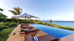 Un espace aménagé au bord de la piscine, avec des chaises longues et des parasols, offrant une vue sur une mer d’un bleu limpide.