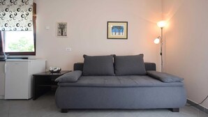 A compact living space with a grey sofa, a small white refrigerator, a floor lamp, and two framed pictures on the wall.