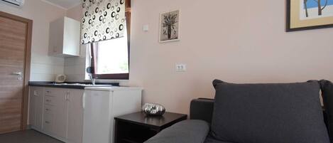 Un espacio habitable compacto con kitchenette, un sofá gris y una mesita.
