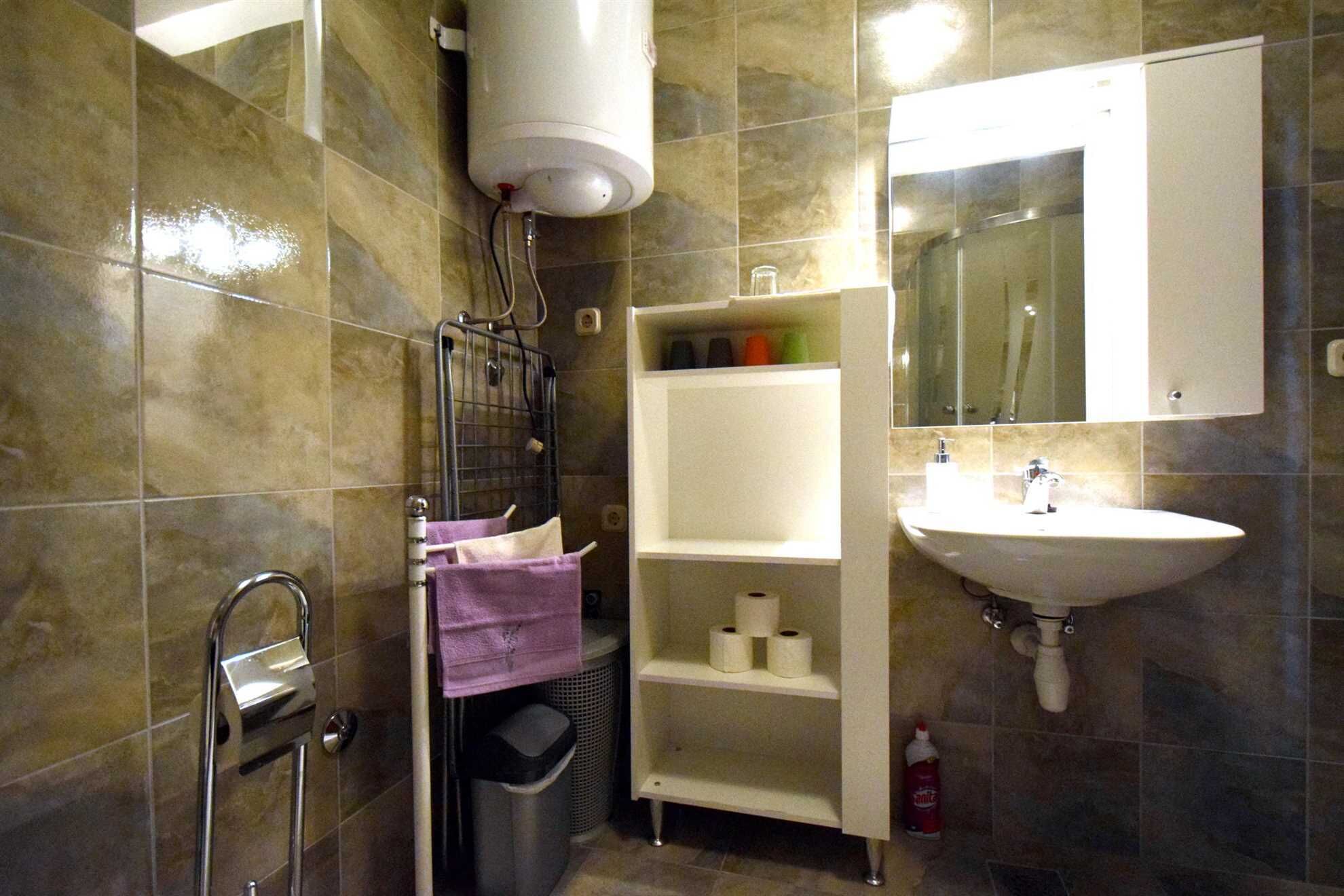 Une salle de bain avec un lavabo blanc, un miroir, un porte-serviettes et une étagère contenant des articles de toilette.