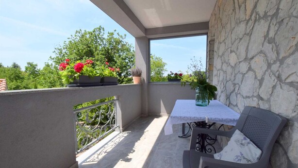 Un balcon avec une table et une chaise, des plantes en pot et un mur en pierre.