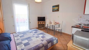 Une chambre de taille modeste comprenant un lit, un téléviseur, une petite table à manger et un coin cuisine.
