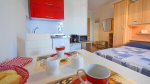 Une petite pièce comprenant un coin cuisine, un lit avec une couette et un placard rouge.