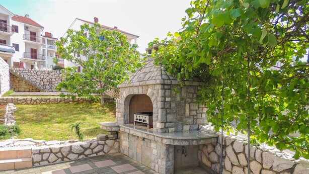 Un espace barbecue extérieur en pierre, doté d’un gril intégré, entouré d’un muret en pierre et d’une terrasse dallée.