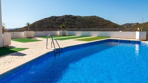 A swimming pool with a metal ladder, surrounded by a white wall and a green lawn area. - Casa Jurinea Beach with sea view and pool (Carboneras)