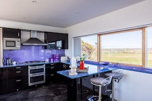 A modern kitchen with a large window, a built-in microwave, and a stove. - Minstrel Lodge : Spacious 4‑Bed Villa Rhosneigr (Rhosneigr)