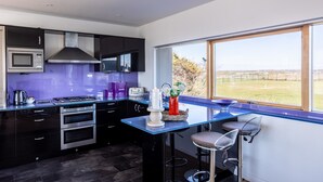 A modern kitchen with a large window, built-in appliances, and a bar area. - Minstrel Lodge : Spacious 4‑Bed Pet-Friendly Villa with Sea Views in Rhosneigr | Managed by Anglesey (Rhosneigr)