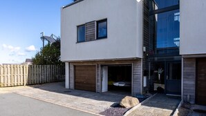 A modern two-story building with a garage and a covered outdoor area. - Minstrel Lodge : Spacious 4‑Bed Pet-Friendly Villa with Sea Views in Rhosneigr | Managed by Anglesey (Rhosneigr)