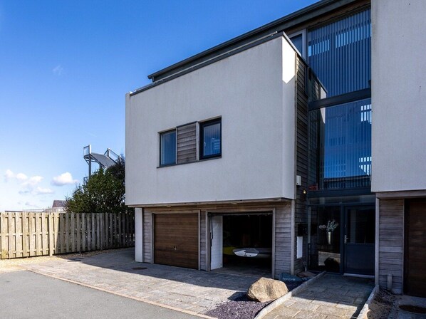 A modern two-story building with a garage, a wooden fence, and a clear sky.