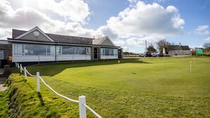 A building with a large windowed facade, a grassy area in front, and a clear sky with clouds. - Minstrel Lodge : Spacious 4‑Bed Pet-Friendly Villa with Sea Views in Rhosneigr | Managed by Anglesey (Rhosneigr)