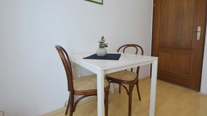 A dining area with a white table, two wooden chairs with woven seats, a vase with flowers, and a framed picture on the wall. - Studio Vera with balcony (Malinska)