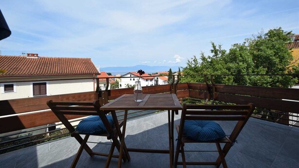 A balcony with two wooden chairs and a table, overlooking a cityscape with red-tiled roofs and greenery. - Studio Vera with balcony (Malinska)