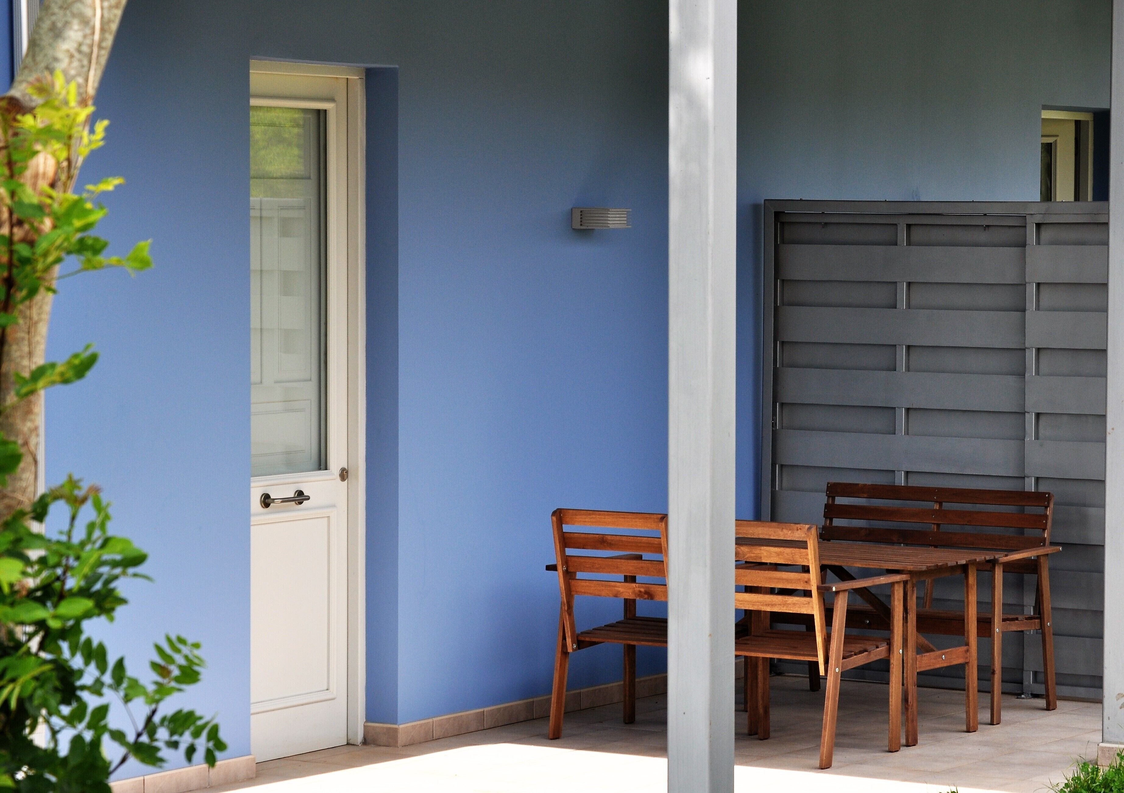 A wooden bench and table set against a blue wall, with a white door and a grey shutter in the background.