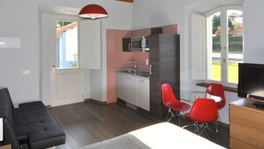 A modern kitchen with white cabinets, a microwave, and a red chair. There is a black sofa and a wooden desk with a television. - Rural apartment Casona la Sierra for 3 people (Cudillero)