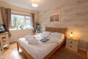 Un dormitorio bien iluminado con una cama de madera, una mesita de noche con lámpara, una ventana con cortinas y un cuadro colgado en la pared.