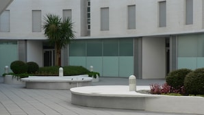 A modern building with a flat roof, rectangular windows, and a central courtyard with a palm tree and shrubs. - BEACH APARTMENT 3 in TOSSA DE MAR (Tossa de Mar)