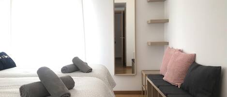 Un dormitorio con dos camas, un banco, un espejo y una ventana con cortinas.
