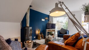 A cozy living room with a fireplace, leather sofa, and a large window. - Driftwood : Pet‑Friendly Seaside Home in Rhosneigr | Managed by Anglesey Holiday Lettings (Rhosneigr)