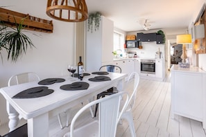 A modern kitchen with white cabinetry, a dining table with black placemats, and a hanging plant.