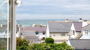 A coastal residential area with houses, a clear sky, and a view of the sea. - Driftwood : Pet‑Friendly Seaside Home in Rhosneigr | Managed by Anglesey Holiday Lettings (Rhosneigr)
