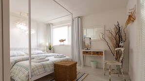 A bedroom with a bed, bedside tables, a dresser, a chair, and a window with curtains. - Driftwood : Pet‑Friendly Seaside Home in Rhosneigr | Managed by Anglesey Holiday Lettings (Rhosneigr)