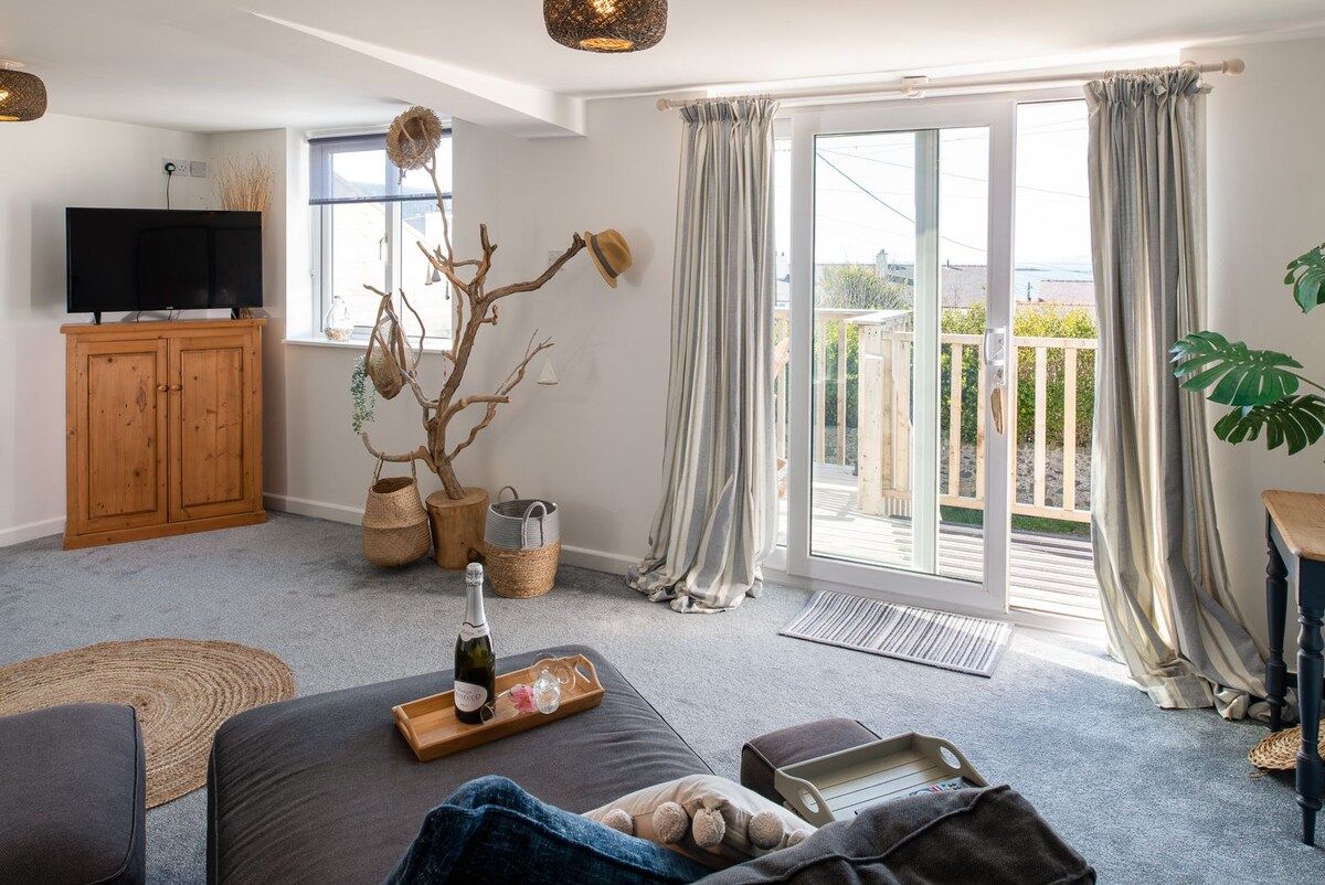 A living room with a sofa, a television, a wooden cabinet, a plant, and a balcony with curtains.