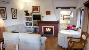A living room with a fireplace, a sofa, a dining table with chairs, and a television. - Self catering Cortijo Algabia for 4 people (Alhendín)