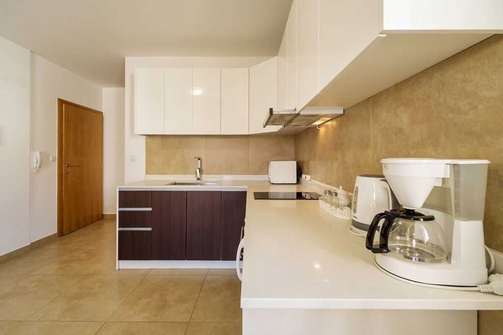 A modern kitchen with white cabinets, a coffee maker, and a sink.