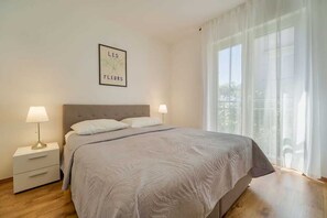 A bedroom with a bed, two bedside tables, a nightstand, a window with curtains, and a wall-mounted picture. - Apartment Nino 2 with balcony (Malinska)