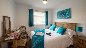 Ein Schlafzimmer mit einem Bett, Nachttischen, einem Schreibtisch, einem Stuhl, einer Heizung und einem Fenster mit Vorhängen.