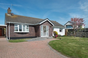 A two-story house with a brick exterior, a front porch, and a well-maintained lawn. - Rhonwil: Pet-friendly 3-bed bungalow in Anglesey (Rhosneigr)