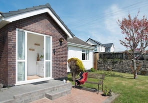 A residential property with a brick facade, a glass door entrance, a small garden with a bench, and a tree with pink blossoms.