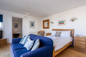 A bedroom with a bed, a blue sofa, a wooden nightstand, and a wall-mounted lamp. - Morwennol: A stunning shore side location with fantastic views (Rhosneigr)