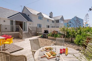 Une terrasse avec une table dressée pour un repas, des sièges d’extérieur et un barbecue.