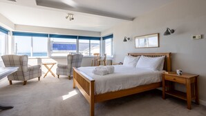 Ein Schlafzimmer mit einem großen Bett, zwei Stühlen, einem kleinen Tisch und einem Fenster mit Blick.