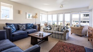 Ein geräumiges Wohnzimmer mit großem Fenster, einem Sofa, einem Couchtisch und einem Korbstuhl.