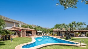 Ein Swimmingpool, umgeben von einer gepflegten Rasenfläche, mit Steingebäuden und Außenbereichen mit Sitzgelegenheiten.