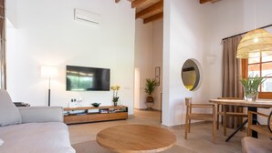 Ein modernes Wohnzimmer mit einer Couch, einem runden Holztisch, einem Fernseher, einem Esstisch mit Stühlen und einem großen Spiegel.