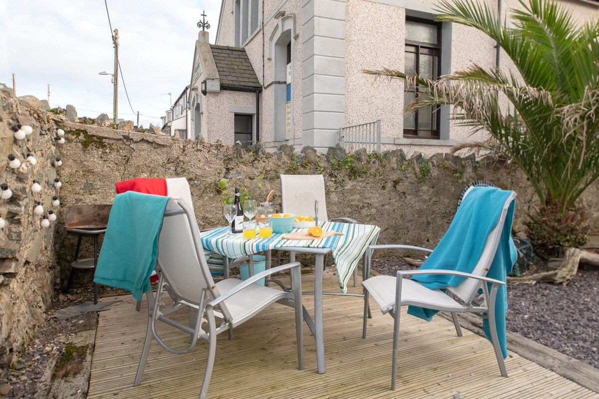 An outdoor dining area with a table set for two, chairs, and a view of a building in the background.