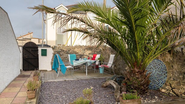 An outdoor patio with a table and chairs, surrounded by potted plants and a palm tree. - Bryn Awel: Family-Friendly 3-Bed Apartment in Rhosneigr | Managed by Anglesey Holiday Lettings (Rhosneigr)