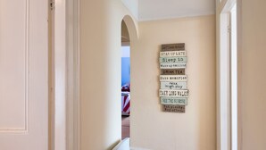 A hallway with a wall-mounted sign listing various activities like 'STAY UP LATE', 'Sleep in', and 'Take long walks'. - Bryn Awel: Family-Friendly 3-Bed Apartment in Rhosneigr | Managed by Anglesey Holiday Lettings (Rhosneigr)