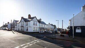 A street view with a row of white buildings, including a shop with a sign that reads "FATFACE." - Bryn Awel: Family-Friendly 3-Bed Apartment in Rhosneigr | Managed by Anglesey Holiday Lettings (Rhosneigr)