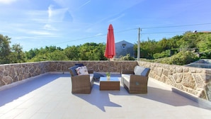 Une terrasse sur le toit, aménagée avec des meubles en osier et un parasol rouge, entourée de murs en pierre et de verdure.