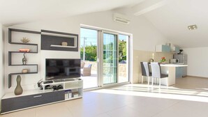 Un salon moderne doté d’un téléviseur à écran plat, d’étagères intégrées et d’une porte-fenêtre coulissante donnant sur un balcon.