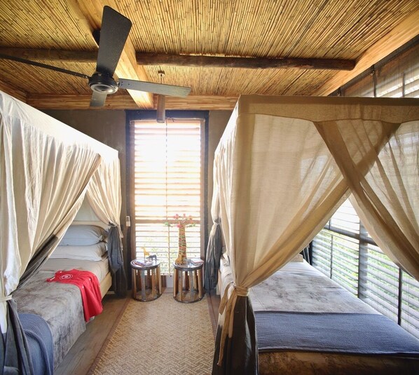Una habitación con dos camas, un ventilador de techo y una pequeña mesa con sillas.