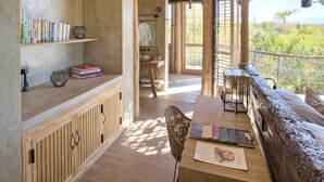 Un'ampia stanza con soffitto in legno, una panca di legno a lato della finestra, un tavolo con una sedia e uno scaffale con libri e oggetti decorativi.